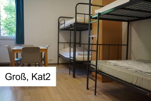 Cette chambre dispose de 3 lits superposés, d'une table et d'une table. dans l'établissement Kiek in AöR Jugendherberge & Hostel, à Neumünster