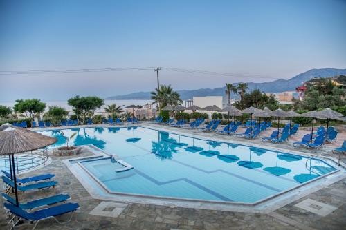 una gran piscina con sillas y sombrillas azules en Semiramis Village, en Hersonissos