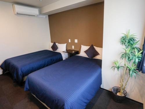 a hotel room with two beds and a plant at HOTEL LiVEMAX Higashi Ginza in Tokyo