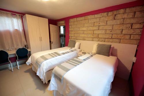a room with two beds and a brick wall at The Stone Guest House in Teyateyaneng