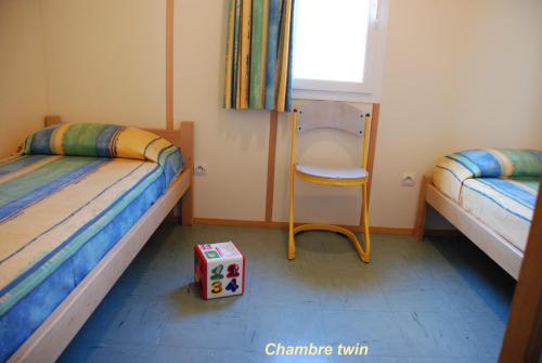 sypialnia z 2 łóżkami, krzesłem i pudełkiem w obiekcie Les Chalets de la MARGERIDE w mieście Blavignac