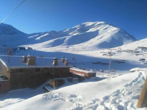 a building in the snow with a mountain in the background at Gite Oukaimeden in Oukkainrdem