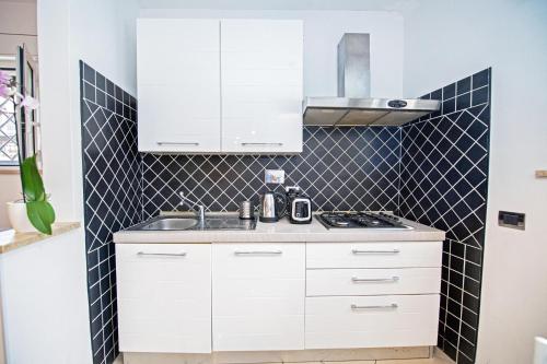 una cocina con armarios blancos y una pared de azulejos negros en B&Bea sweet home Aurelia, en Roma