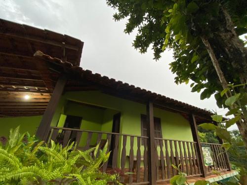 uma casa verde com varanda e árvores em Pouso das Folhas em Tiradentes