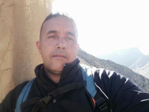 a man wearing a scarf standing next to a wall at Gite Oukaimeden in Oukkainrdem