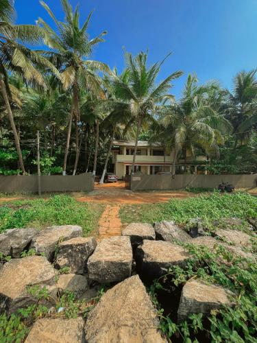 a house with palm trees and rocks in front of it at Kizhunna rock beach house in Kannur