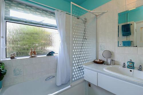 a bathroom with a tub and a sink and a window at Whitestones in Brighstone