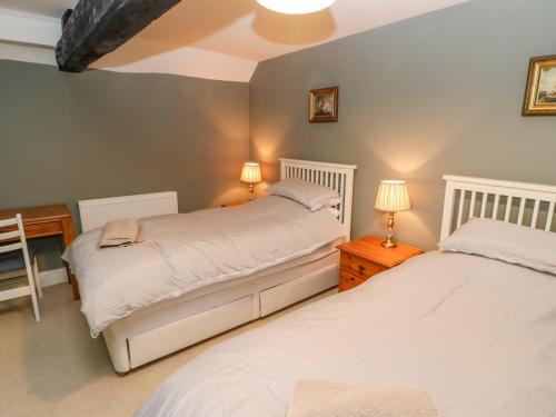 two beds in a bedroom with two lamps and a table at Firkin Cottage in Bedale