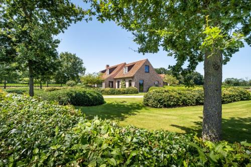 een huis op een gazon met een boom en struiken bij Hoeve den Akker - luxueuze vakantiewoningen met privétuinen nabij Brugge, Damme, Knokke, Sluis en Cadzand in Damme