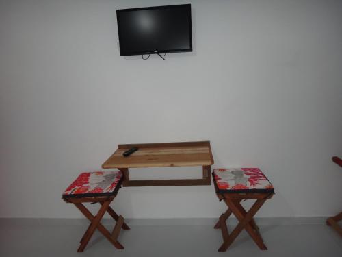 a table and two chairs with a tv on a wall at Urbano Suítes in Ubatuba