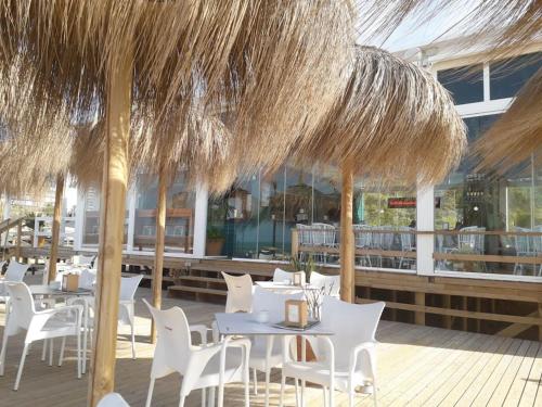 a restaurant with white tables and chairs and straw umbrellas at Precioso piso en la playa in El Puerto de Santa María