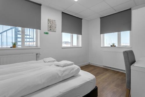 a white bedroom with a large bed and windows at Bank Guesthouse by KEF Airport in Keflavík