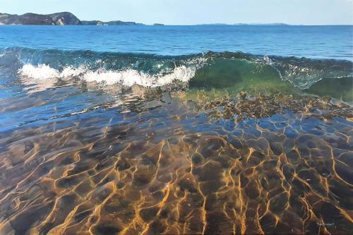 a wave breaking on a beach with rocks in the water at Stanmore Bay Beachfront Cottage in Whangaparaoa