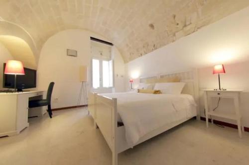 a white bedroom with a large bed and a desk at Le Malve Cave Retreat in Matera