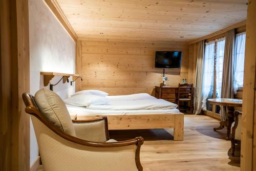a bedroom with a bed and a chair and a television at Posthotel Rössli in Gstaad