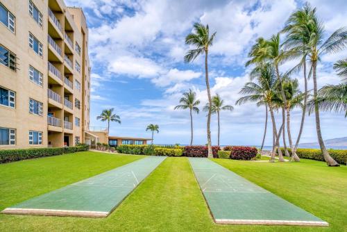 a tennis court in front of a building with palm trees at Menehune Shores by Coldwell Banker Island Vacations in Kihei