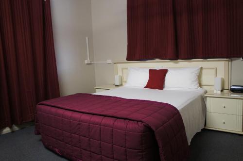 a bedroom with a large bed with red curtains at Ayrline Motel in Ayr