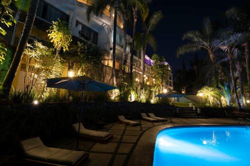 a pool with chairs and an umbrella next to a building at Hotel Grand Vista Cuernavaca in Cuernavaca