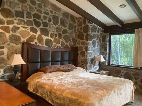Un dormitorio con una pared de piedra y una cama grande. en Agradable casa rural con piscina privada, en Yautepec