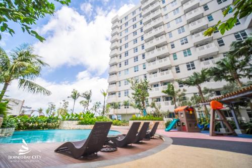 a hotel with a pool and chairs in front of a building at Apartement Borneo Bay Tower kartanegara Balikpapan in Balikpapan