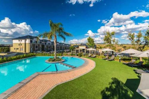 a pool at a resort with a palm tree at Modern 3-bed Garden Apartment in Waterfall in Midrand