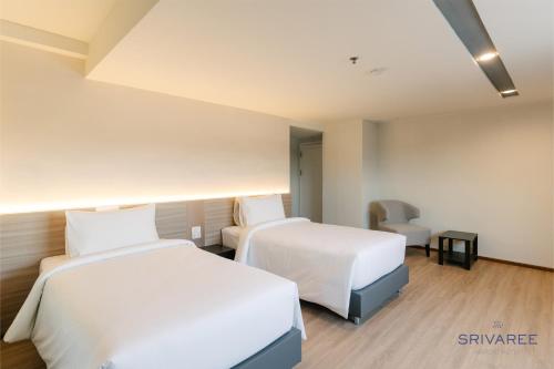 ein Hotelzimmer mit 2 Betten und einem Stuhl in der Unterkunft The Srivaree Airport Hotel in Samutprakarn