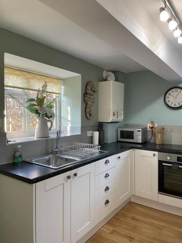 a kitchen with white cabinets and a sink and a clock at Chiddy Nook Cottage in Chideock