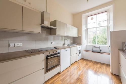 a kitchen with white cabinets and a large window at Beautiful 2 Bed 2 Bath Flat overlooking Meadows Park in Edinburgh