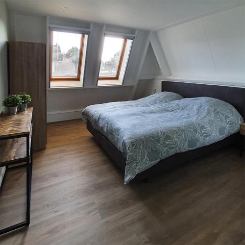 a bedroom with a bed and a table and two windows at B&B Kamille in Delden