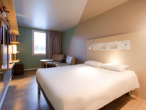 a hotel room with a large white bed and a chair at ibis budget Albertville in Gilly-sur-Isère