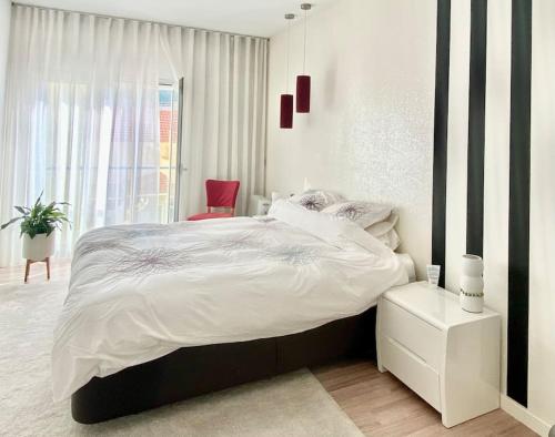 um quarto branco com uma cama grande e uma cadeira vermelha em Riverside - apartment em Cruz Quebrada