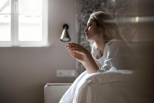 a woman sitting in a bed looking out a window at HOTEL & SPA Goldene Rose in Dinkelsbühl
