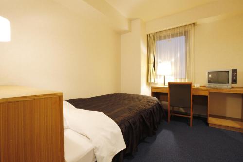 a hotel room with a bed and a desk and a television at Sankei City Hotel Hachioji in Hachioji