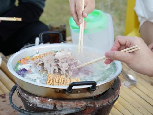 une personne qui cuisine de la nourriture dans un pot avec des baguettes dans l'établissement Yellowstone Camps O2 Zone Khao Kho, à Khao Kho