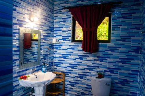 baño con paredes de azulejos azules, lavabo y ventana en Les Elles Guesthouse Self Catering en Baie Lazare Mahé