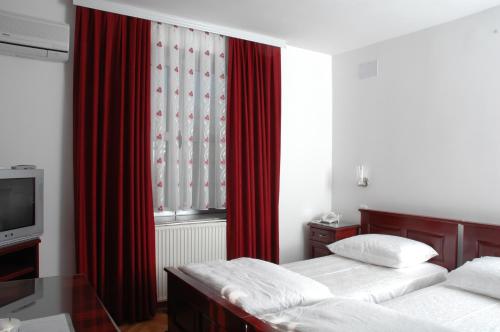 two beds in a room with red curtains and a tv at Vila Lux Milikic in Kraljevo