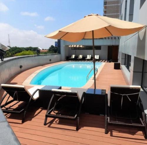 a swimming pool with chairs and an umbrella on a deck at Hotel Express in Luanda