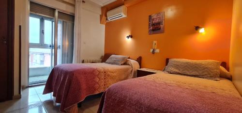 2 camas en una habitación con paredes de color naranja y ventana en Hostal Ramón y Cajal en Valladolid