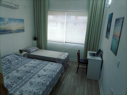 um quarto com 2 camas, uma secretária e uma janela em Ponta da Praia amplo 3dorm 3ban frente ao mar em Santos