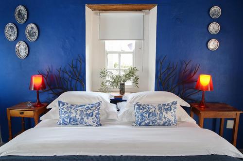 a blue bedroom with a large white bed with pillows at Dennehof Karoo Guesthouse in Prince Albert