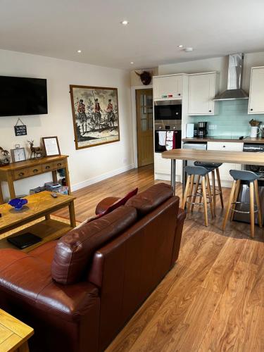 a living room with a leather couch and a kitchen at Lesanne Cottage in Inverness