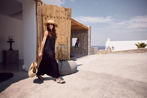 a woman in a black dress and hat holding a bird cage at Amazon Mykonos Suites & Spa in Agios Ioannis Mykonos
