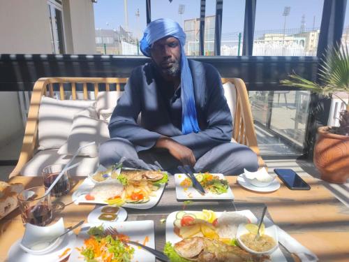 Ein Mann sitzt auf einem Stuhl mit Essen auf einem Tisch. in der Unterkunft transit in Nouakchott