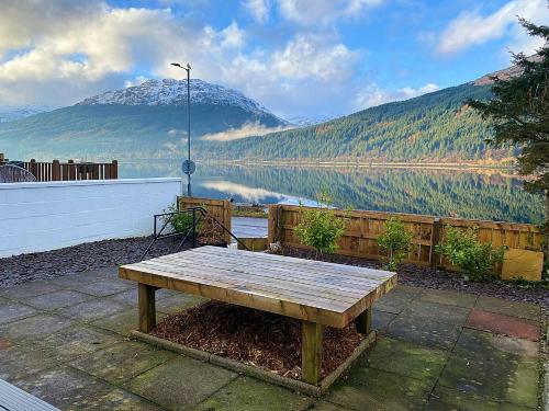 a wooden bench sitting next to a body of water at MacLeen Cottage in Arrochar