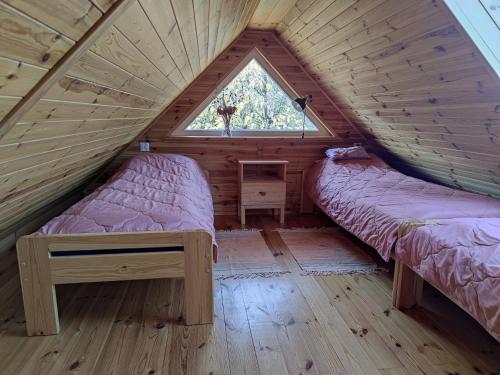 two beds in a wooden room with a window at KTA TARPAN Mały Domek in Masiewo