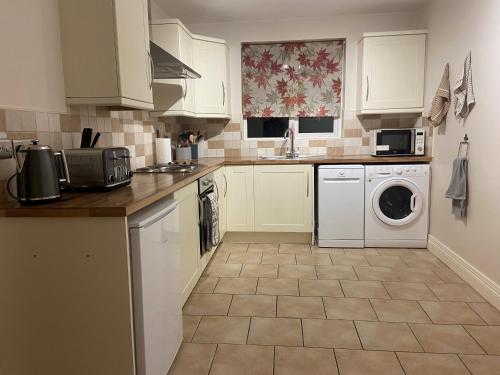 uma cozinha com armários brancos e uma máquina de lavar e secar roupa em Glenbann House em Coleraine