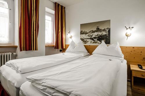 two beds in a bedroom with white sheets at HOTEL B&B MARILENA in Arabba