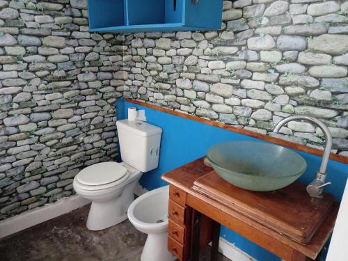 baño con lavabo, aseo y pared de piedra en La Casita de Carla en Quequén