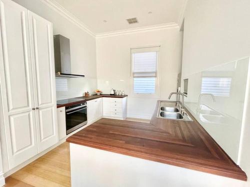 uma cozinha com armários brancos e um balcão de madeira em Garden Cottage em Geelong