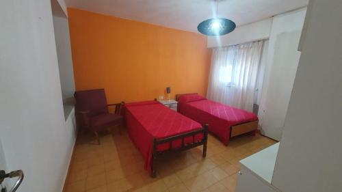 Zimmer mit 2 roten Betten sowie einem Tisch und Stühlen in der Unterkunft Habitacion economica con estacionamiento Necochea in Necochea